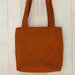 May include: A brown corduroy tote bag with two wide straps. The bag is made of a soft, textured fabric.