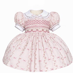 May include: A pink and white striped dress with a white collar and puff sleeves. The bodice features intricate embroidery, and the skirt is adorned with floral and bow patterns. The dress is designed for a child.