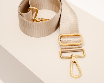 May include: A beige woven strap with gold hardware, including a rectangular buckle and a swivel clasp.