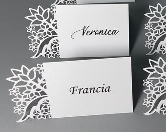May include: Five white place cards with decorative floral cutouts on the left side. The names "Lotaro", "Veronica", "Francia", "Dylan", and "Angello Varronni" are written in black ink on the cards.