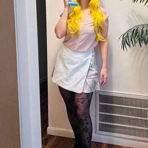 May include: A woman wearing a white skirt, black tights with a floral pattern, and black heeled boots. She is holding a blue phone to her ear and wearing a blue paper hat shaped like a phone.