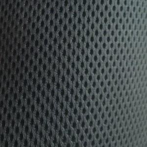 May include: Close-up of a dark grey mesh fabric with a repeating pattern of oval-shaped holes. The texture appears soft and flexible, suitable for various applications.