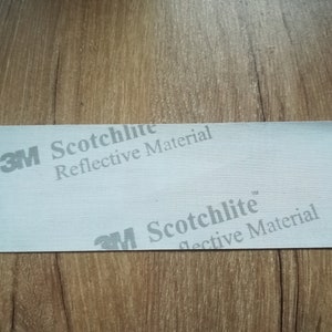 May include: A close-up of a white reflective material tape with the text "3M Scotchlite Reflective Material" printed on it.