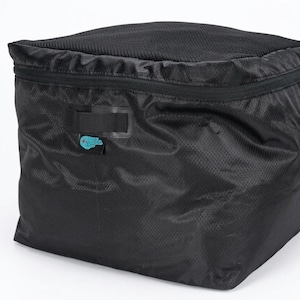 May include: Black, square-shaped storage bag with a mesh top and a zipper closure. The bag has a textured pattern and a small, blue tag. The zipper is white. The bag has a handle on the side.