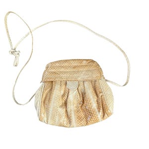 May include: A cream-colored, vintage crossbody bag with a textured snakeskin pattern. The bag has a rounded shape with a flap closure and a long, thin strap. The strap is knotted at the top.