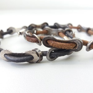 May include: Two leather bracelets with silver bike chain links. The bracelets are brown and black.
