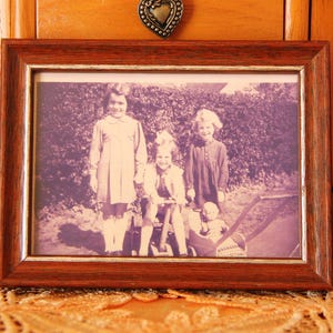 Puede incluir: Una fotograf&iacute;a en sepia enmarcada con cuatro ni&ntilde;os. El marco de madera tiene un acabado marr&oacute;n oscuro. La fotograf&iacute;a muestra a tres ni&ntilde;as y un beb&eacute; en un cochecito. El marco descansa sobre un mantel de encaje naranja.