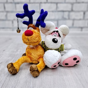 Könnte beinhalten: Ein Plüsch-Rentier mit blauen Geweih und einer Glocke, das neben einer weißen Plüschmaus mit schwarzen Augen und einem gelb-schwarz gestreiften Shirt sitzt.