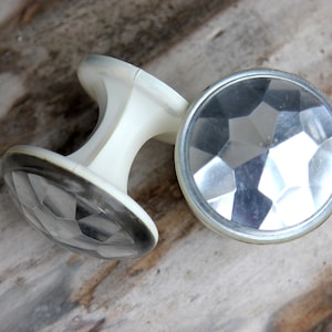 May include: Two white plastic drawer knobs with clear, faceted glass inserts. The knobs have a simple, classic design.