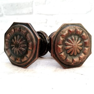 Może przedstawiać: Dwa antyczne, ośmiokątne gałki drzwiowe z ozdobnym wzorem kwiatowym w miedzianym wykończeniu.