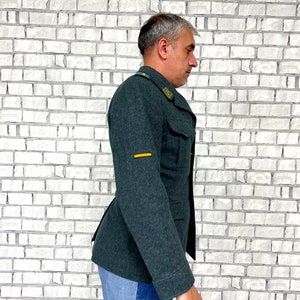 May include: A dark green military-style jacket with a yellow stripe on the sleeve. The jacket has a button closure and two pockets on the front.