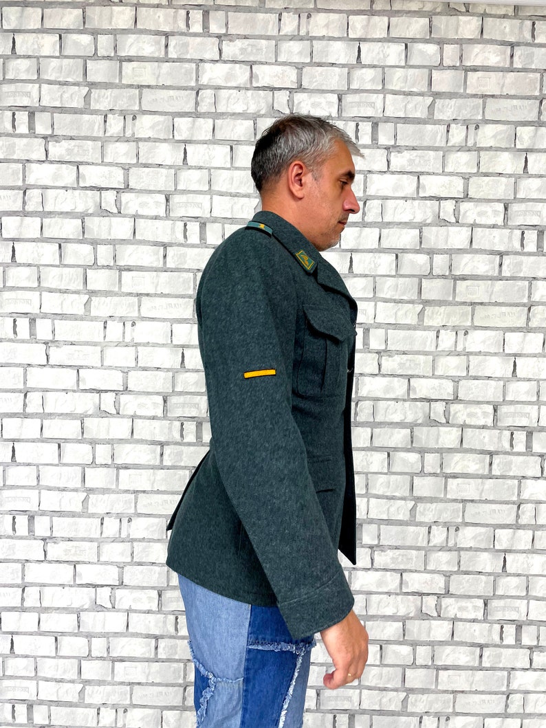May include: A dark green military-style jacket with a yellow stripe on the sleeve. The jacket has a button closure and two pockets on the front.