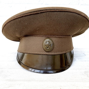 Op de afbeelding: Een bruine militaire pet met een zwart vizier en een gouden sterembleem.