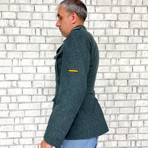 May include: A dark green military jacket with a yellow stripe on the sleeve. The jacket is made of a thick, textured fabric.