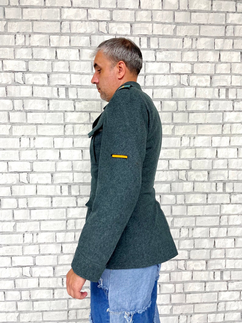 May include: A dark green military jacket with a yellow stripe on the sleeve. The jacket is made of a thick, textured fabric.