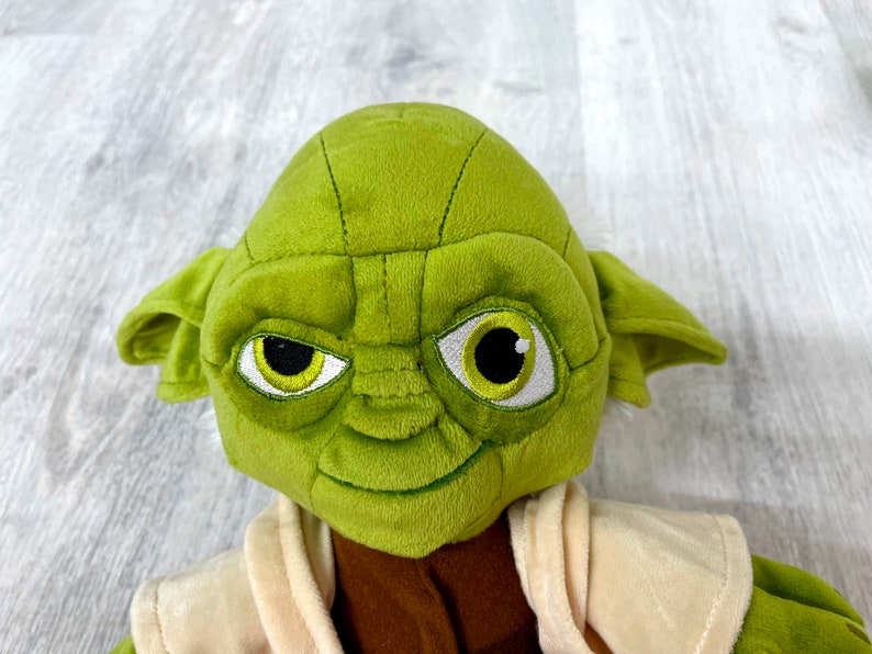 May include: Green plush Yoda toy with large ears, brown eyes, and a white robe.