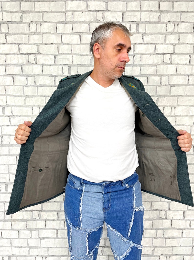 May include: A dark green jacket with a brown lining. The jacket has a pocket on the inside and a label with the text "50 69" on the inside. The jacket is open and a person is wearing it.