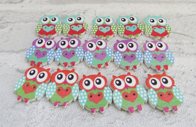 May include: A set of 18 wooden owl buttons with colorful polka dot and heart patterns. The owls have big eyes and are painted in shades of green, blue, purple, red, and white.