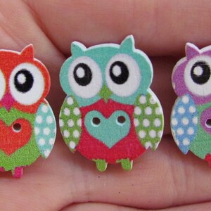 May include: Three wooden owl buttons with polka dot patterns and heart-shaped centers. The owls are in shades of red, blue, and purple.