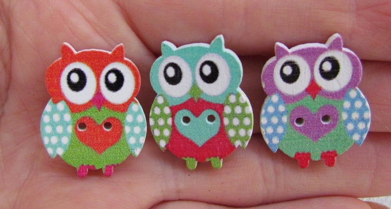 May include: Three wooden owl buttons with polka dot patterns and heart-shaped centers. The owls are in shades of red, blue, and purple.