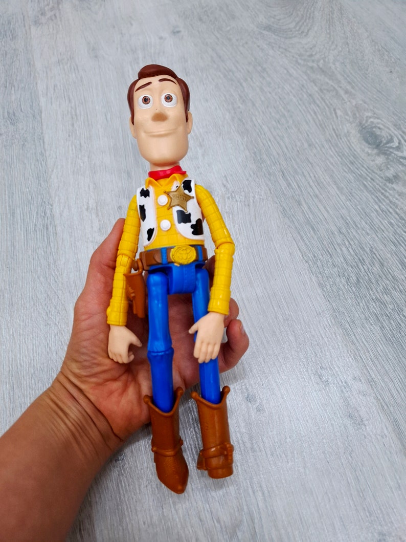 Puede incluir: Una figura de juguete de pl&aacute;stico de Woody de la franquicia Toy Story. Woody lleva su caracter&iacute;stico sombrero de vaquero, chaleco y pantalones vaqueros. Tiene una expresi&oacute;n amistosa en la cara y est&aacute; extendiendo el brazo derecho.