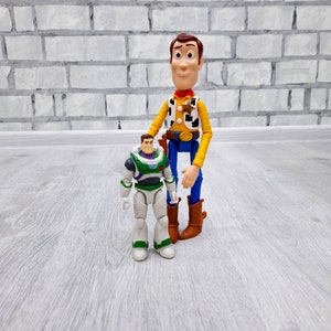 Puede incluir: Los personajes de Toy Story, Woody y Buzz Lightyear. Woody es un mu&ntilde;eco vaquero con un sombrero marr&oacute;n, una camisa amarilla, un chaleco azul y botas marrones. Buzz Lightyear es un ranger espacial con un traje blanco y verde, un casco azul y una visera verde.