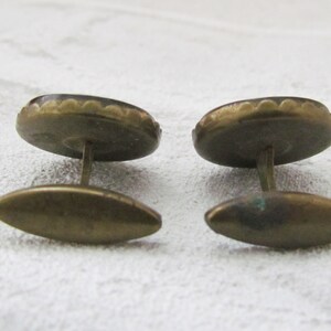 May include: A pair of gold cufflinks with a dark brown oval-shaped stone set in a scalloped metal frame.