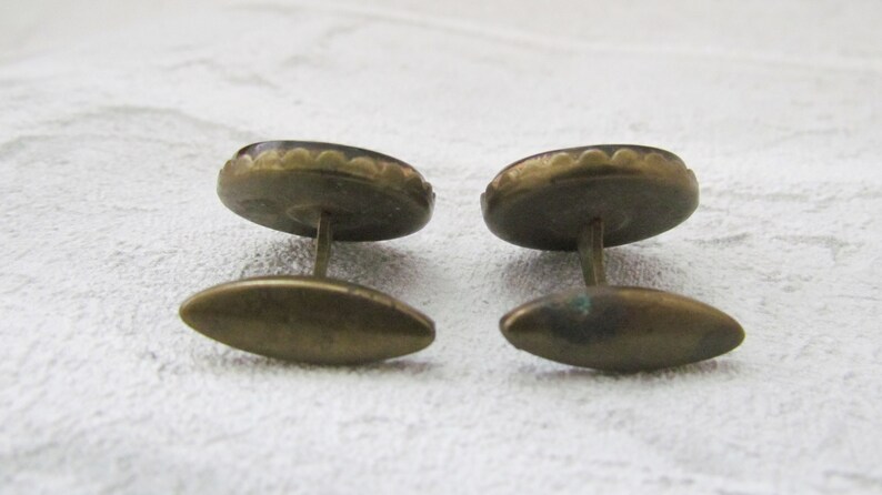 May include: A pair of gold cufflinks with a dark brown oval-shaped stone set in a scalloped metal frame.