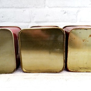 May include: Three vintage red metal canisters with gold lids. The canisters are empty and have a worn, vintage look.