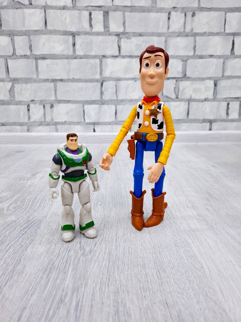 Puede incluir: Los personajes de Toy Story, Woody y Buzz Lightyear. Woody lleva su caracter&iacute;stico sombrero de vaquero y chaleco, mientras que Buzz est&aacute; en su traje de ranger espacial. Est&aacute;n de pie sobre un suelo de madera gris claro.