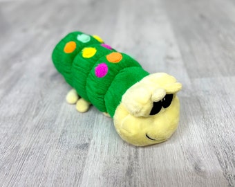 May include: A green plush caterpillar toy with yellow, pink, and blue polka dots. The caterpillar has a yellow head with black eyes and a smiling mouth.