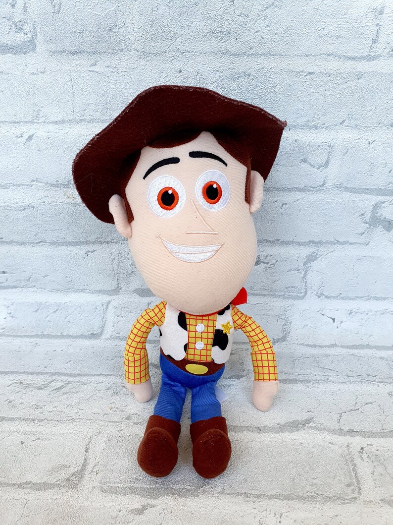 May include: A plush toy of Woody from the Toy Story franchise. Woody is wearing his signature brown hat, red and yellow plaid shirt, and blue jeans. He has a friendly smile and brown eyes.