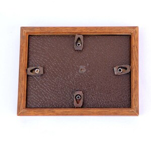 Puede incluir: Un marco de fotos rectangular de madera, visto desde atr&aacute;s, con un respaldo marr&oacute;n y herrajes met&aacute;licos para colgar. El marco est&aacute; hecho de madera de tonos c&aacute;lidos y tiene un dise&ntilde;o simple y cl&aacute;sico. La parte posterior tiene una apariencia texturizada similar al cuero.