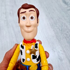 Puede incluir: Una figura de juguete de pl&aacute;stico amarillo y marr&oacute;n de Woody de la franquicia Toy Story. Woody lleva un pa&ntilde;uelo rojo, un chaleco amarillo con estampado de vaca blanco y negro, un cintur&oacute;n marr&oacute;n con hebilla dorada y pantalones vaqueros azules. Lleva una insignia de estrella de sheriff dorada en su chaleco que dice "Sheriff".