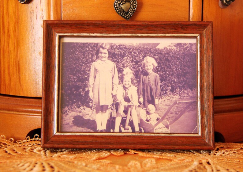 Puede incluir: Una fotograf&iacute;a en sepia enmarcada con cuatro ni&ntilde;os. El marco de madera tiene un acabado marr&oacute;n oscuro. La fotograf&iacute;a muestra a tres ni&ntilde;as y un beb&eacute; en un cochecito. El marco descansa sobre un mantel de encaje naranja.