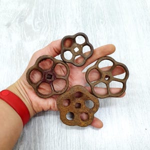 Peut inclure: Quatre poignées de vannes antiques en métal rouillé, avec un motif en forme de fleur. Les poignées sont de couleur brun foncé et ont une forme circulaire avec plusieurs trous. Le fond est un grain de bois gris clair.