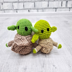 May include: Two crocheted Yoda characters, one green and one brown, with black eyes and white accents.