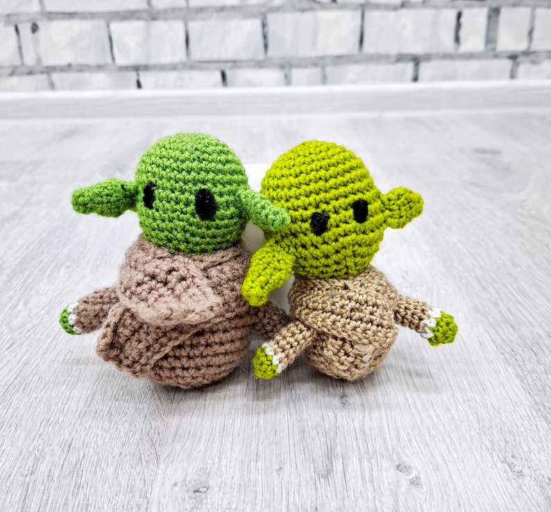 May include: Two crocheted Yoda characters, one green and one brown, with black eyes and white accents.