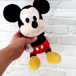 May include: A plush Mickey Mouse toy with black ears, a black nose, and red shorts with white polka dots. The toy is holding a white glove in its right hand.