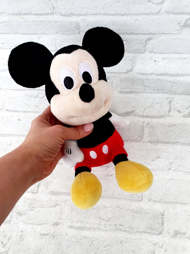 May include: A plush Mickey Mouse toy with black ears, a black nose, and red shorts with white polka dots. The toy is holding a white glove in its right hand.