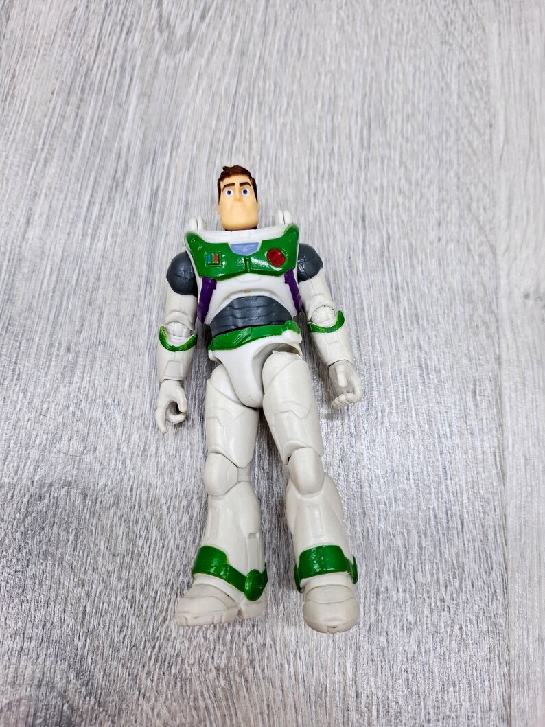 Puede incluir: Una figura de acci&oacute;n de pl&aacute;stico blanco y verde de Buzz Lightyear de la franquicia Toy Story. La figura tiene el pelo marr&oacute;n y un traje espacial verde y blanco con un bot&oacute;n rojo en el pecho.