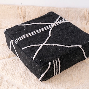 May include: Black and white geometric patterned floor cushion. The cushion is made of a soft, textured fabric and has a square shape.