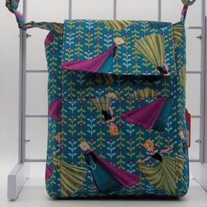 Peut inclure: Un sac &agrave; bandouli&egrave;re bleu sarcelle avec une fermeture &agrave; rabat. Le sac est en tissu avec un motif de feuilles vertes et de fleurs roses. Le sac pr&eacute;sente un imprim&eacute; de personnages du film La Reine des Neiges.
