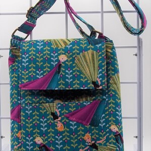 Peut inclure: Un sac &agrave; bandouli&egrave;re bleu sarcelle avec une fermeture &agrave; rabat. Le sac est d&eacute;cor&eacute; d'un motif r&eacute;p&eacute;t&eacute; de personnages de La Reine des Neiges, dont Elsa et Anna, portant leurs robes caract&eacute;ristiques. Le sac a une bandouli&egrave;re rose et violette.