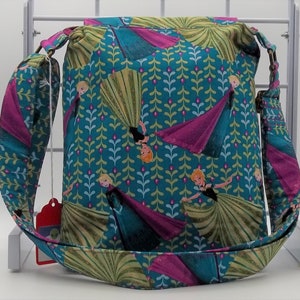 Peut inclure: Un sac en tissu bleu sarcelle avec un motif floral rose et vert repr&eacute;sentant des princesses du film La Reine des Neiges. Le sac a une longue bandouli&egrave;re r&eacute;glable.