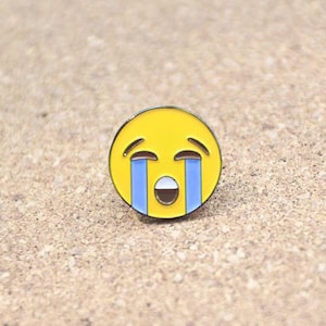 Puede incluir: Pin de emoji amarillo con una cara triste y lágrimas azules. El emoji está llorando y tiene la boca muy abierta.