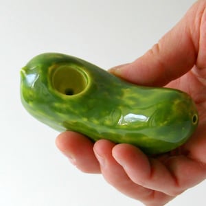 May include: A green ceramic pickle-shaped pipe with a hole for smoking.