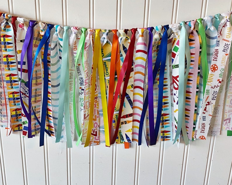 May include: A colorful fabric banner with various patterns and colors, including red, orange, yellow, green, blue, purple, and white. The banner has the words "DESIGN MIX", "PASTE BRUSH SCRUMBLE", "Crayola", and "PASTE CREATE" printed on it.
