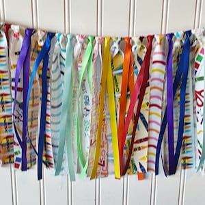 May include: A colorful fabric banner with a rainbow of colors, including green, yellow, orange, red, blue, purple, and white. The banner is made of fabric strips with different patterns, including stripes, polka dots, and solid colors.
