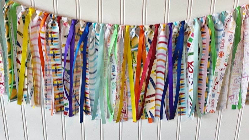 May include: A colorful fabric banner with a rainbow of colors, including green, yellow, orange, red, blue, purple, and white. The banner is made of fabric strips with different patterns, including stripes, polka dots, and solid colors.